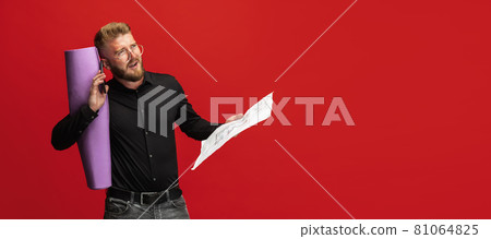 Portrait of funny bearded man, builder, designer or architect with professional equipment isolated on red studio background. Portrait of funny bearded man, builder, designer or architect with professional equipment isolated on red studio background. 81064825