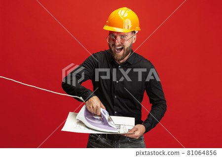 Portrait of funny bearded man, builder, designer or architect with professional equipment isolated on red studio background. Portrait of funny bearded man, builder, designer or architect with professional equipment isolated on red studio background. 81064856