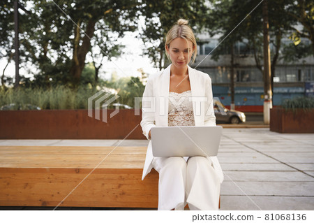 Young beautiful businesswoman working on laptop, sitting on the bench in the street Young beautiful businesswoman working on laptop, sitting on the bench in the street 81068136