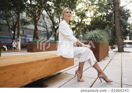 Young attractive businesswoman sitting on wooden bench in a street Young attractive businesswoman sitting on wooden bench in a street 81068143