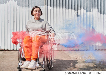 Girl with lower body disability sitting at wheelchair and holding bombs with colored smoke 81068679