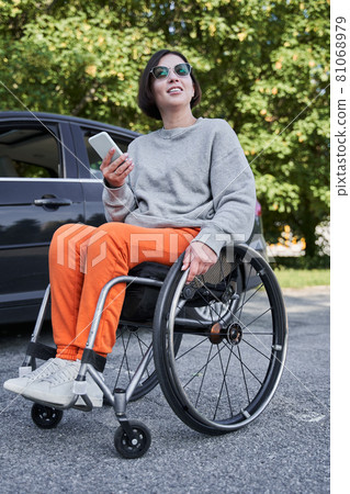 Handicapped woman sitting at the special armchair and holding her smartphone 81068979