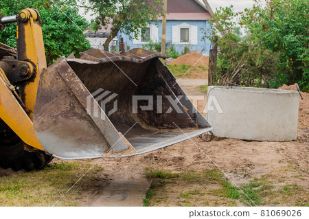 A bucket of a tractor or a bulldozer against a concrete sewer ring. Construction or repair of sewerage in an industrial zone A bucket of a tractor or a bulldozer against a concrete sewer ring. Construction or repair of sewerage in an industrial zone 81069026