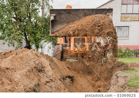 A bucket of a bulldozer fills the trench with earth in an industrial zone. Excavation construction works A bucket of a bulldozer fills the trench with earth in an industrial zone. Excavation construction works 81069028