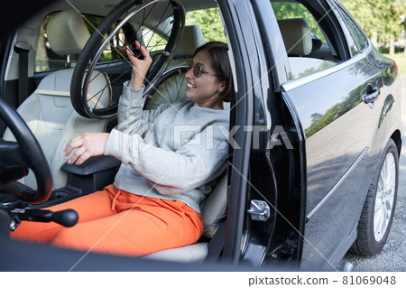 Woman holding her wheelchair while sitting in car on city street and folding it 81069048