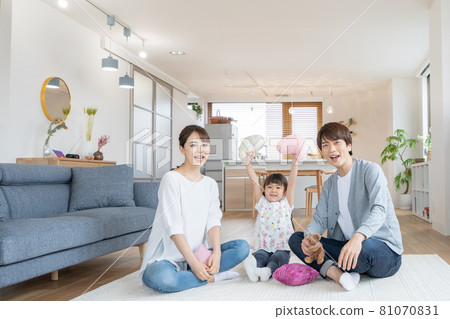 A family of three, an elementary school girl, dad and mom relaxing in the living room 81070831