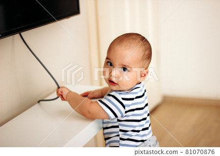 Sweet naughty baby boy pulls the electric cord from the TV 81070876