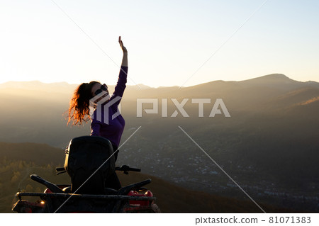 Happy woman driver enjoying extreme riding on ATV quad motorbike in summer mountains at sunset. 81071383