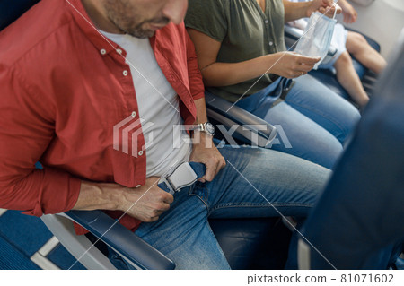 High angle view of male passenger fastening seat belt while sitting on the airplane for safe flight High angle view of male passenger fastening seat belt while sitting on the airplane for safe flight 81071602