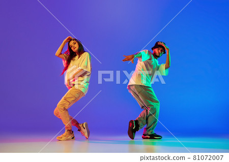 Two young people, guy and girl in casual clothes dancing contemporary dance, hip-hop over blue background in neon light. 81072007