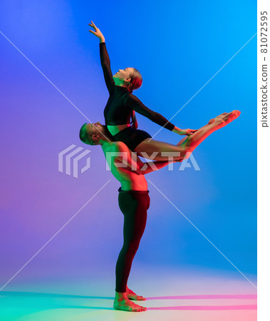 Stylish sportive caucasian couple, male and female dancer dancing contemporary dance on colorful gradient blue pink background in neon light. Stylish sportive caucasian couple, male and female dancer dancing contemporary dance on colorful gradient blue pink background in neon light. 81072595