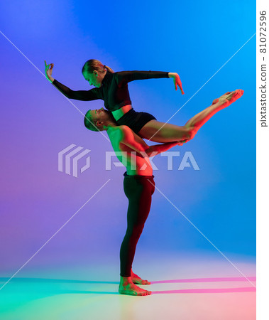 Stylish sportive caucasian couple, male and female dancer dancing contemporary dance on colorful gradient blue pink background in neon light. Stylish sportive caucasian couple, male and female dancer dancing contemporary dance on colorful gradient blue pink background in neon light. 81072596