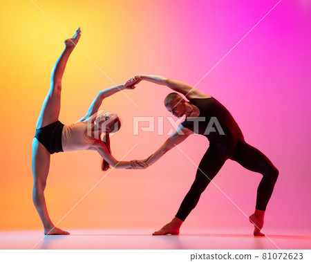 Two dancers, stylish sportive couple, male and female models dancing contemporary dance on colorful gradient yellow pink background in neon light. Two dancers, stylish sportive couple, male and female models dancing contemporary dance on colorful gradient yellow pink background in neon light. 81072623