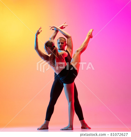 Two dancers, stylish sportive couple, male and female models dancing contemporary dance on colorful gradient yellow pink background in neon light. Two dancers, stylish sportive couple, male and female models dancing contemporary dance on colorful gradient yellow pink background in neon light. 81072627