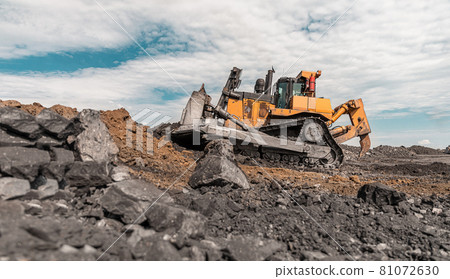 Yellow excavator in career moves overburden. Bulldozer combs the ground, with the bright sun and nice blue sky in the background 81072630