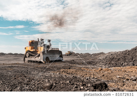 Yellow excavator in career moves overburden. Bulldozer combs the ground, with the bright sun and nice blue sky in the background 81072631