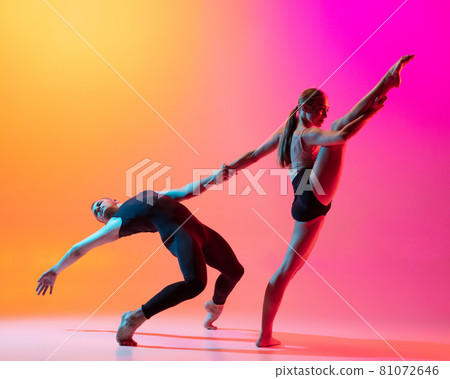 Two dancers, stylish sportive couple, male and female models dancing contemporary dance on colorful gradient yellow pink background in neon light. Two dancers, stylish sportive couple, male and female models dancing contemporary dance on colorful gradient yellow pink background in neon light. 81072646