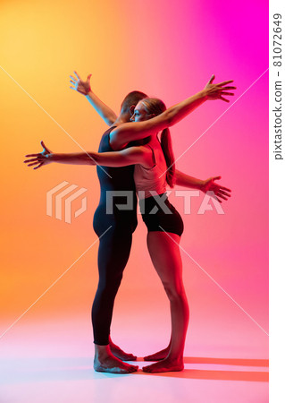 Two dancers, stylish sportive couple, male and female models dancing contemporary dance on colorful gradient yellow pink background in neon light. Two dancers, stylish sportive couple, male and female models dancing contemporary dance on colorful gradient yellow pink background in neon light. 81072649