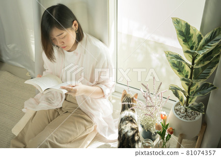 still at home concept with asian woman reading book and play with her cat in her living room still at home concept with asian woman reading book and play with her cat in her living room 81074357