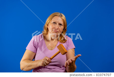 Pretty middle aged woman posing with a kitchen wooden mallet isolated on blue studio background. 81074707