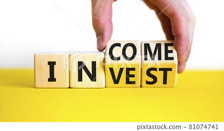 Invest or income symbol. Businessman turns wooden cubes and changes the word 'invest' to 'income'. Beautiful yellow table, white background, copy space. Business and invest or income concept. 81074741