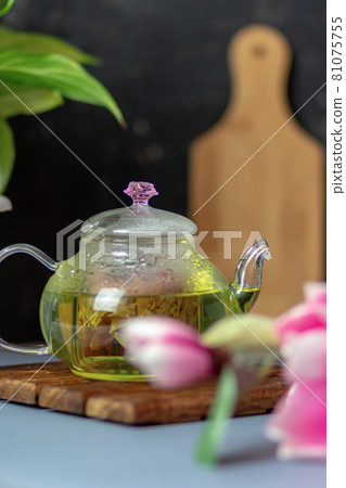 green tea with rose petals in a transparent teapot on a wooden table on a black background. The background is blurred. Tea drinking. green tea with rose petals in a transparent teapot on a wooden table on a black background. The background is blurred. Tea drinking. 81075755