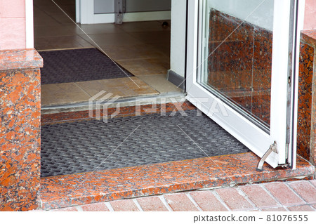 open plastic entrance doors with glass with rubber foot mat close-up of building architecture with granite facade shop entry, nobody. 81076555
