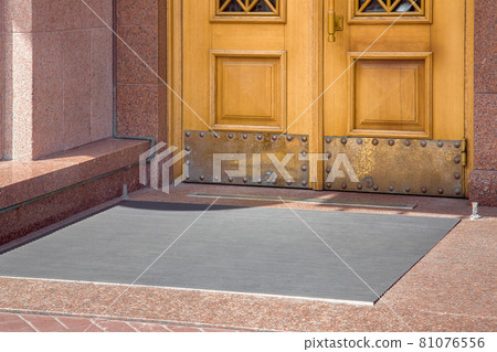 stone entrance with foot mat at the entry door made of wood and granite stone facade cladding of retro European architecture building closeup side view on sunny day, nobody. stone entrance with foot mat at the entry door made of wood and granite stone facade cladding of retro European architecture building closeup side view on sunny day, nobody. 81076556