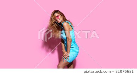 Young woman wearing sunglasses and dress posing on pink studio background 81076681