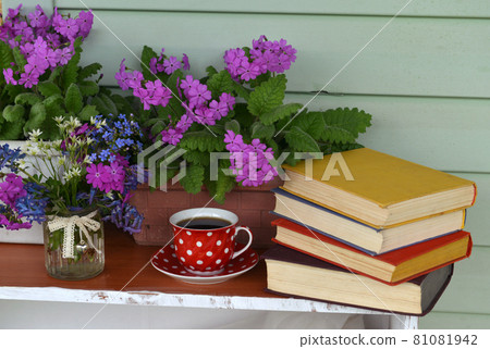 Still life with spring flowers in pot, cup of tea and books with colorful covers. Vintage romantic concept outside in the garden Still life with spring flowers in pot, cup of tea and books with colorful covers. Vintage romantic concept outside in the garden 81081942