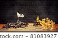 Dark chess raises a white flag in surrender to bright chess on a chessboard and smoke floating in the air and dark brick background. The concept of business loss and bankruptcy. 81083927