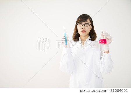 一個穿著實驗室外套的年輕女人,帶著一個燒瓶和一個斜著抬頭的考官 一個穿著實驗室外套的年輕女人,帶著一個燒瓶和一個斜著抬頭的考官 81084601