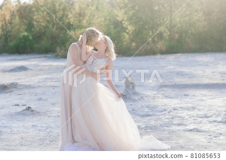 Beautiful lesbian couple walking on sand along river bank on their wedding day Beautiful lesbian couple walking on sand along river bank on their wedding day 81085653