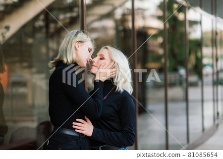 Two young females walking smiling embracing and kissing outdoor in the city Two young females walking smiling embracing and kissing outdoor in the city 81085654