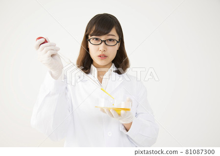 A young woman in a lab coat pouring reagents into a petri dish with a pipette 81087300