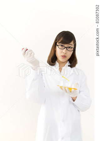 A young woman in a lab coat pouring reagents into a petri dish with a pipette 81087302