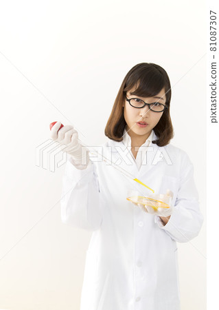 A young woman in a lab coat pouring reagents into a petri dish with a pipette 81087307