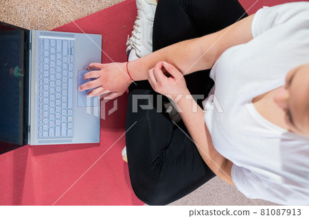 A chubby young woman is watching an online fitness lesson on a laptop. Distance sports training. A chubby young woman is watching an online fitness lesson on a laptop. Distance sports training. 81087913