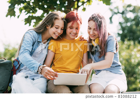 Three teenage girls communicate with their friends and classmates via video link using a laptop in the park. Friends, friendship, time together Three teenage girls communicate with their friends and classmates via video link using a laptop in the park. Friends, friendship, time together 81088212