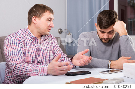 Friend calming distressed guy at home table Friend calming distressed guy at home table 81088251