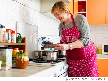 Mature woman housewife during cooking soup at her kitchen Mature woman housewife during cooking soup at her kitchen 81088591