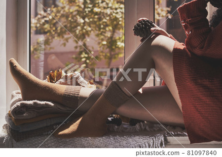 Cold autumn days - a young multi-racial female drinks coffee in a cozy windowsill. Middle-eastern or mixed-race woman enjoys weekend drinking hot tea near the windows 81097840