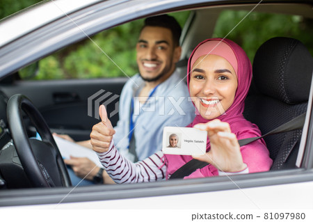 Happy muslim woman sitting in car with instructor and showing driver license Happy muslim woman sitting in car with instructor and showing driver license 81097980