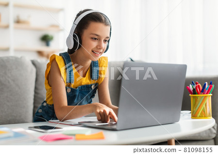 Girl sitting at desk, typing on keyboard, wearing headphones 81098155