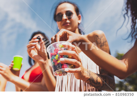 Young beautiful women in swimsuits resting on the beach, drinking cool drinks, having fun, sunbathing 81098350