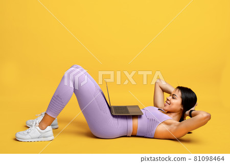Online gym. Fit african american lady doing abs exercise sit-ups, training with laptop, exercising on yellow background Online gym. Fit african american lady doing abs exercise sit-ups, training with laptop, exercising on yellow background 81098464