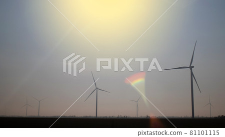Windmills in the fog near a field of sunflowers. Early morning. See the movement of the blades, as a strong wind is blowing. Wind turbine are installed at different distances and hidden in the fog Windmills in the fog near a field of sunflowers. Early morning. See the movement of the blades, as a strong wind is blowing. Wind turbine are installed at different distances and hidden in the fog 81101115