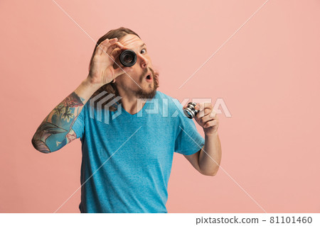 Portrait of young man, photographer, cameraman with camera lens having fun isolated on pink studio background. Concept of occupation, job, funny meme emotions Portrait of young man, photographer, cameraman with camera lens having fun isolated on pink studio background. Concept of occupation, job, funny meme emotions 81101460