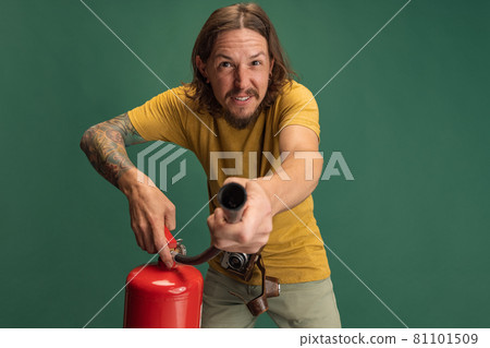 Comic portrait of young man with fire extinguisher having fun isolated on green studio background. Concept of occupation, job, funny meme emotions Comic portrait of young man with fire extinguisher having fun isolated on green studio background. Concept of occupation, job, funny meme emotions 81101509