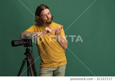 Comic portrait of young man, photographer, cameraman with retro camera having fun isolated on green studio background. Concept of occupation, job, funny meme emotions Comic portrait of young man, photographer, cameraman with retro camera having fun isolated on green studio background. Concept of occupation, job, funny meme emotions 81101517